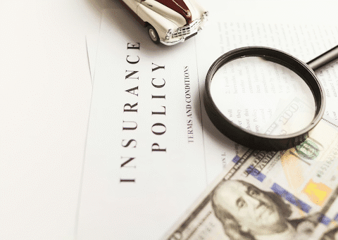 An image of an insurance policy on a desk with money next to it and a magnifying glass.